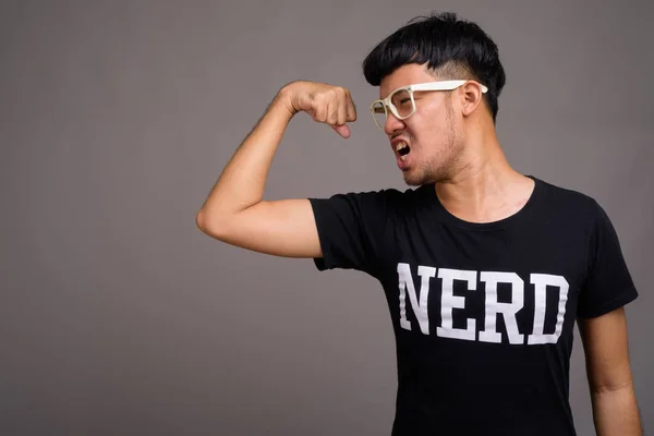 Joven asiática nerd hombre usando anteojos contra gris fondo —  Fotos de Stock