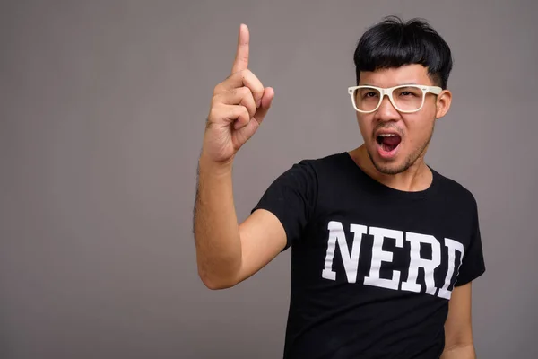 Junger asiatischer Nerd mit Brille vor grauem Hintergrund — Stockfoto