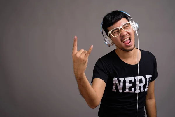 Jeune asiatique nerd homme écoute de la musique sur fond gris — Photo