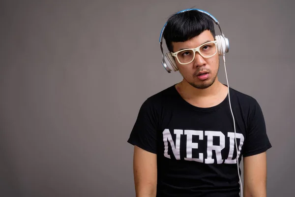 Fiatal ázsiai kocka férfi hallgat zenét szemben szürke háttér — Stock Fotó