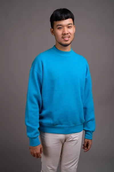 Portret van jonge Aziatische man tegen grijze achtergrond — Stockfoto