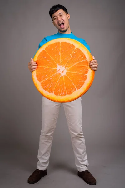 Porträt eines jungen asiatischen Mannes mit einem großen Stück Orange — Stockfoto