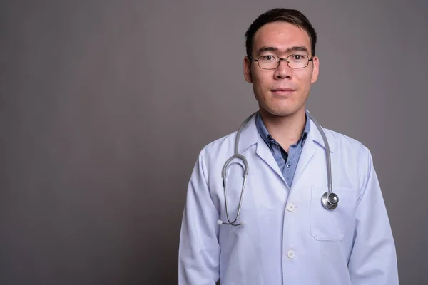 Joven asiático hombre médico contra gris fondo —  Fotos de Stock