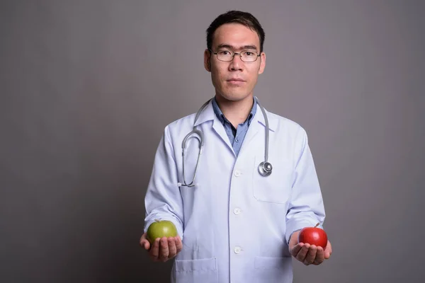 Joven asiático hombre médico contra gris fondo —  Fotos de Stock