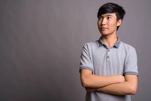 Jeune homme asiatique portant un polo gris sur fond gris — Photo