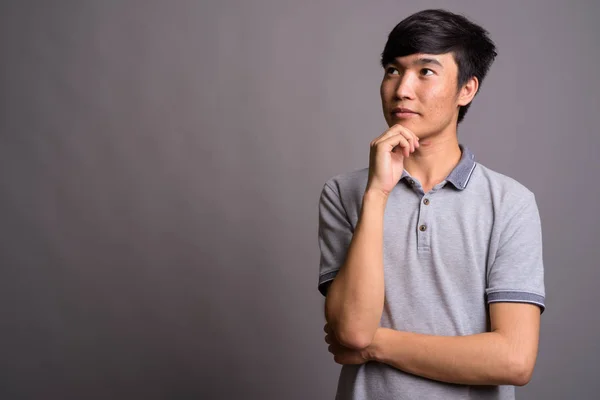 Jonge Aziatische man draagt grijze polo shirt tegen grijze achtergrond — Stockfoto