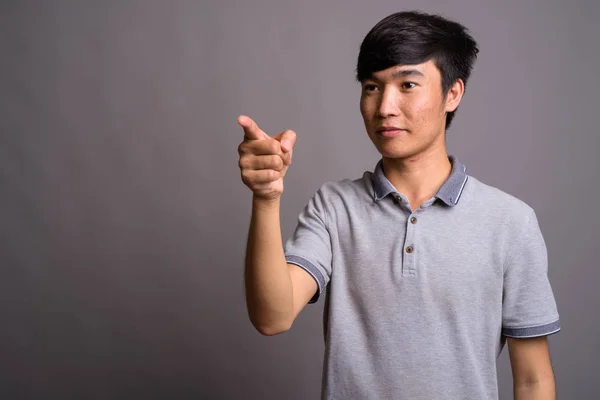 Jeune homme asiatique portant un polo gris sur fond gris — Photo