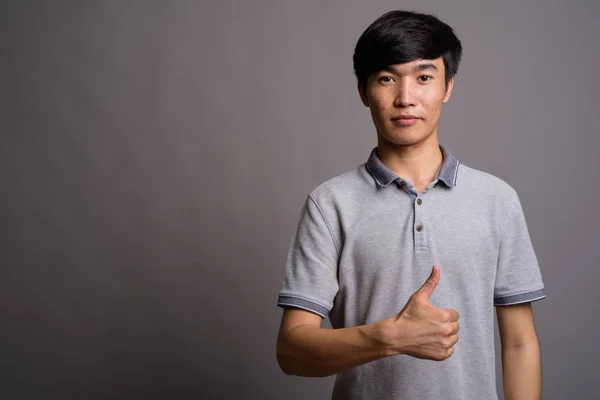 Молодий азіат у сірій сорочці поло на сірому фоні. — стокове фото