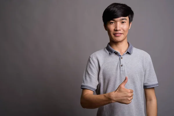 Молодой азиат в серой рубашке для поло на сером фоне — стоковое фото