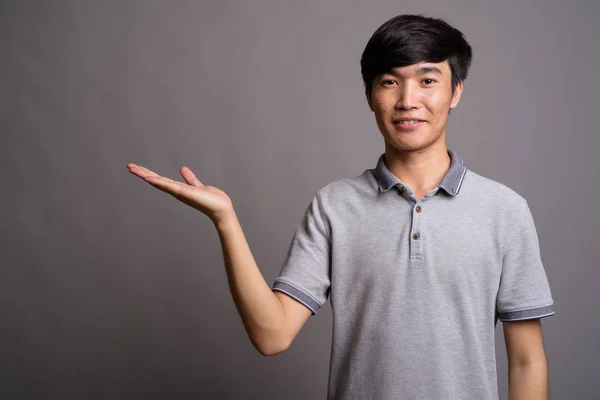 Joven asiático vestido con polo gris sobre fondo gris — Foto de Stock