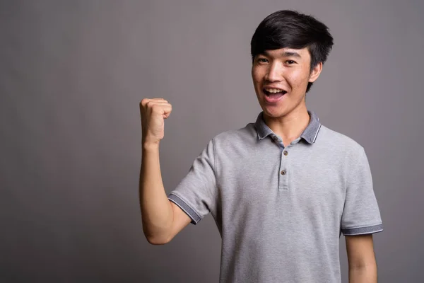 Jonge Aziatische man draagt grijze polo shirt tegen grijze achtergrond — Stockfoto