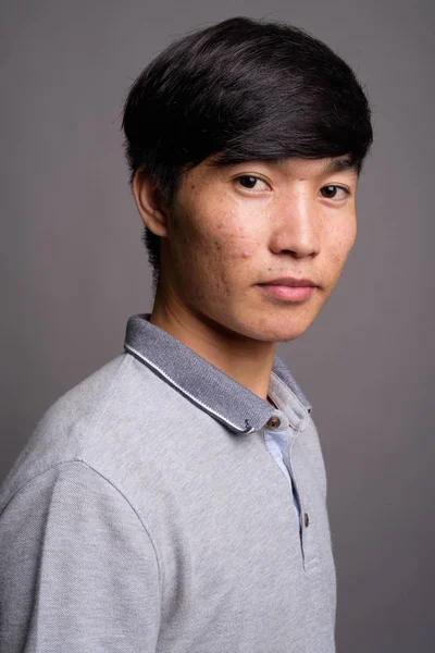 Ung asiatisk man bär grå pikétröja mot grå bakgrund — Stockfoto