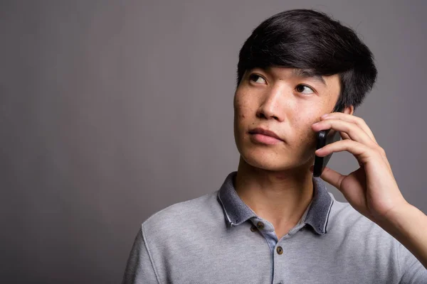 Mladý asijský muž pomocí mobilního telefonu na šedém pozadí — Stock fotografie