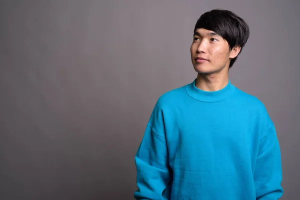 Genç Asyalı adam gri arka planda mavi kazak giyiyor. — Stok fotoğraf