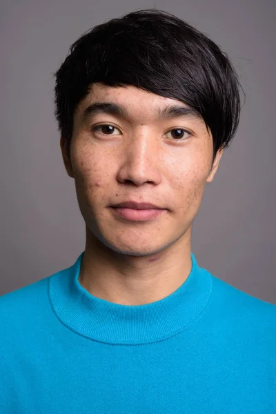 Junger Asiate trägt blauen Pullover vor grauem Hintergrund — Stockfoto