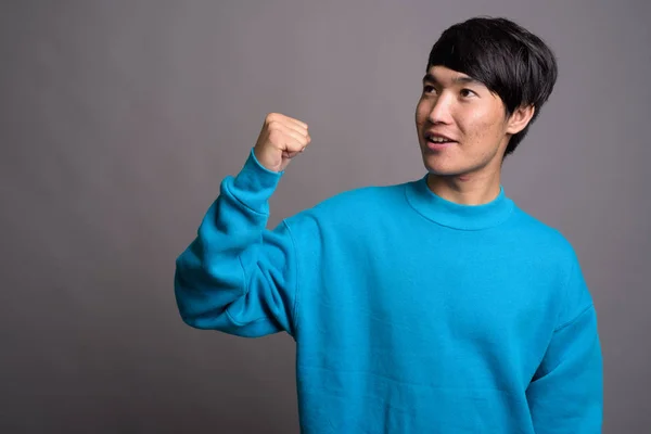 Νεαρός Ασιάτης φοράει μπλε πουλόβερ σε γκρι φόντο — Φωτογραφία Αρχείου
