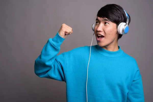 Mladý asijský muž poslech hudby na šedém pozadí — Stock fotografie