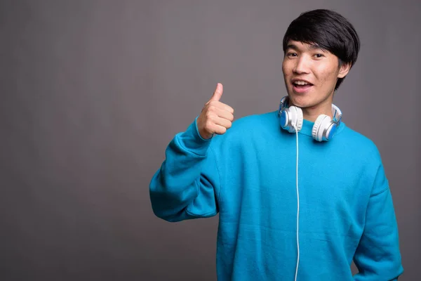 在灰色背景下戴耳机的亚洲年轻人 — 图库照片