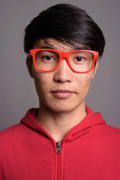 Fiatal ázsiai ember ellen szürke szemüveg viselése piros kabát — Stock Fotó
