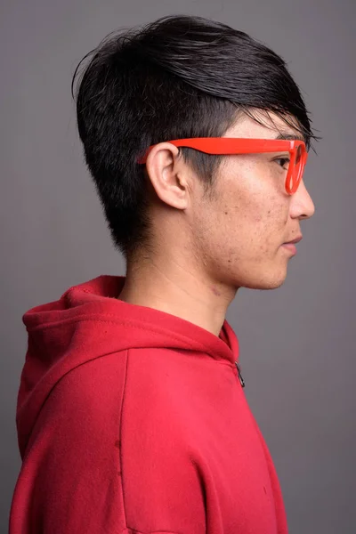 Ung asiatisk man bär röd jacka med glasögon mot grå — Stockfoto