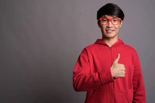 Jovem ásia homem vestindo vermelho jaqueta com óculos contra cinza — Fotografia de Stock