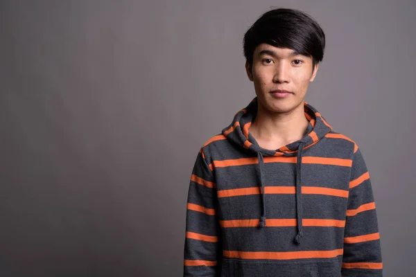 Gri arka planda çizgili kapüşonlu genç Asyalı adam — Stok fotoğraf