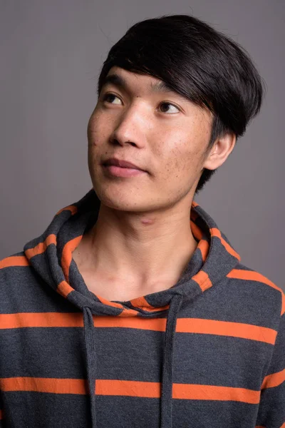 Giovane uomo asiatico indossa felpa con cappuccio a righe contro sfondo grigio — Foto Stock