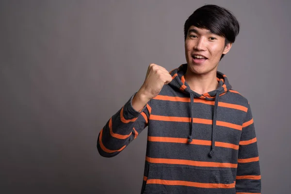 Junger Asiate trägt gestreiften Kapuzenpulli vor grauem Hintergrund — Stockfoto
