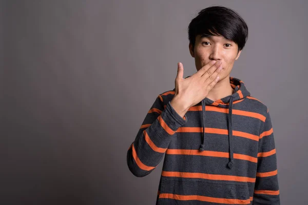 Joven hombre asiático con sudadera con capucha rayada sobre fondo gris —  Fotos de Stock
