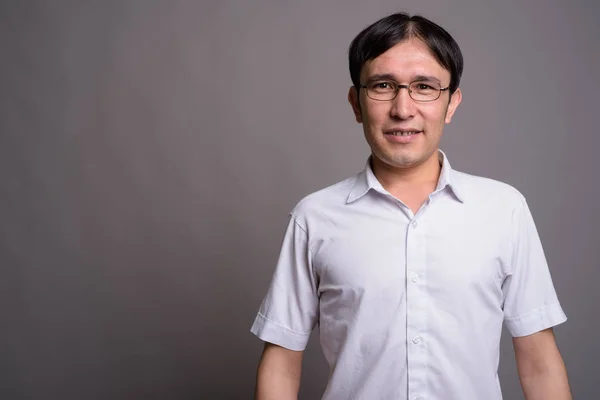 Mladý asijský nerd muž nosí brýle proti šedému pozadí — Stock fotografie