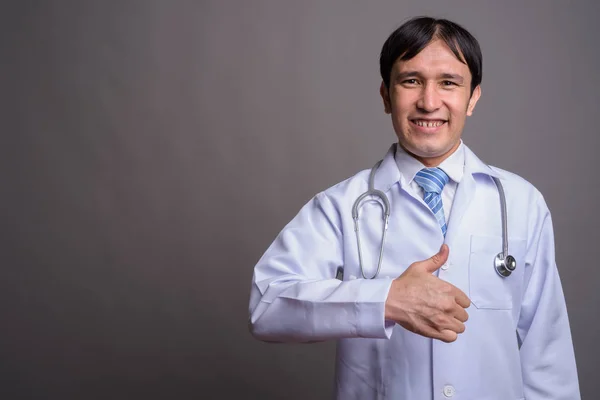 Joven asiático hombre médico contra gris fondo — Foto de Stock