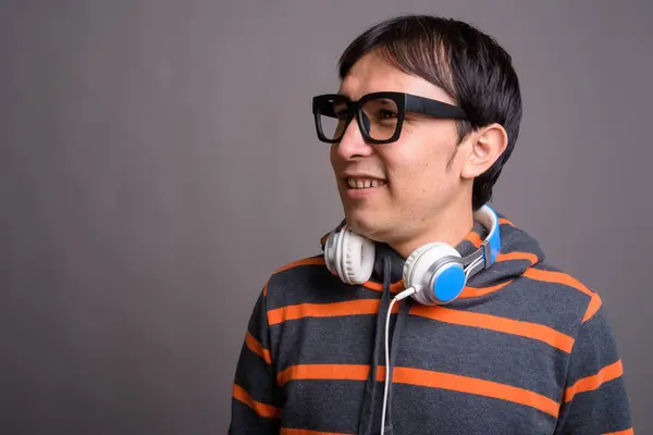 Joven asiático nerd hombre usando sudadera con capucha y auriculares contra gris —  Fotos de Stock