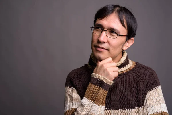 Young Asian nerd man wearing turtleneck sweater against gray bac