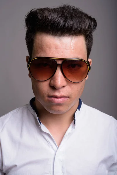 Fiatal ázsiai üzletember szürke háttérb ellen napszemüveget visel — Stock Fotó