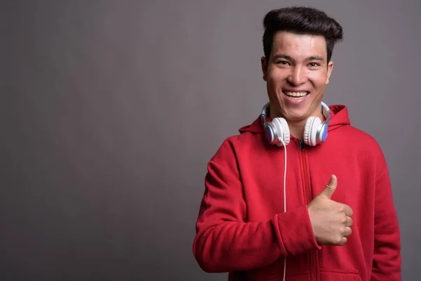 Joven asiático hombre usando auriculares contra fondo gris — Foto de Stock