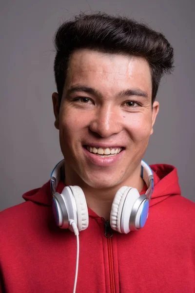 Mladý asijský muž nosí sluchátka na šedém pozadí — Stock fotografie