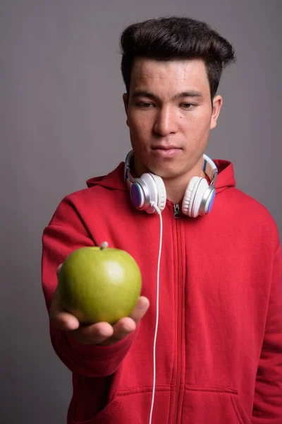 Jovem homem asiático usando fones de ouvido contra fundo cinza — Fotografia de Stock