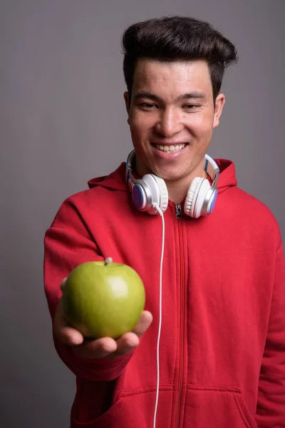 Young Asian man wearing headphones against gray background — Stock Photo, Image