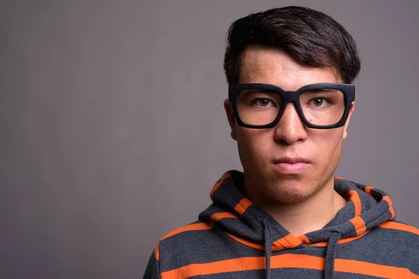 Joven asiático nerd hombre usando sudadera con capucha contra gris fondo — Foto de Stock