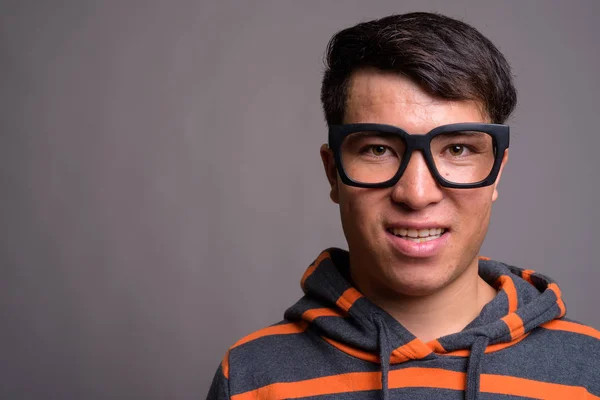 Joven asiático nerd hombre usando sudadera con capucha contra gris fondo — Foto de Stock