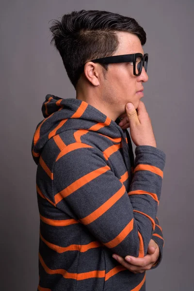 Jovem ásia nerd homem vestindo hoodie contra cinza fundo — Fotografia de Stock