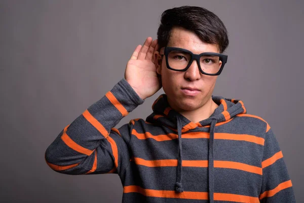 Mladý asijský nerd muž nosí mikinu proti šedému pozadí — Stock fotografie