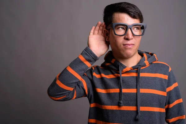Young Asian nerd man wearing hoodie against gray background