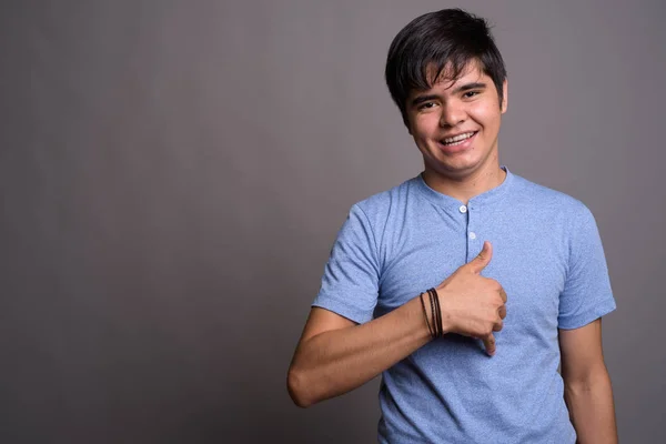 Jonge Aziatische tiener jongen blauw shirt tegen grijze CHTERGRO dragen — Stockfoto