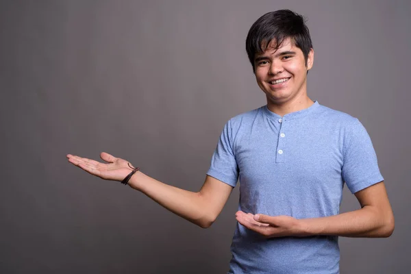 Joven adolescente asiático vistiendo camisa azul contra fondo gris — Foto de Stock