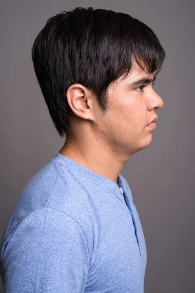 Joven adolescente asiático vistiendo camisa azul contra fondo gris — Foto de Stock