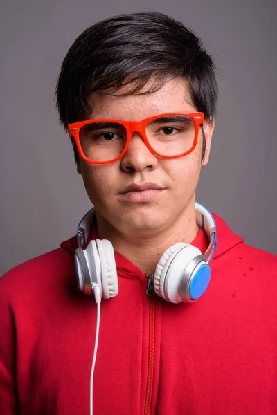 亚洲少年穿着红色夹克 配上红色眼镜和灰色背景耳机的工作室照片 — 图库照片