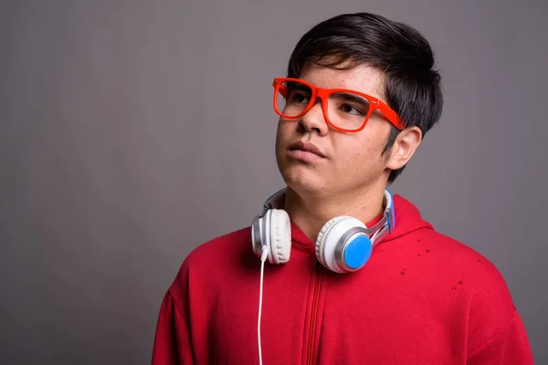 Jovem ásia adolescente menino vestindo fones de ouvido contra cinza backgrou — Fotografia de Stock