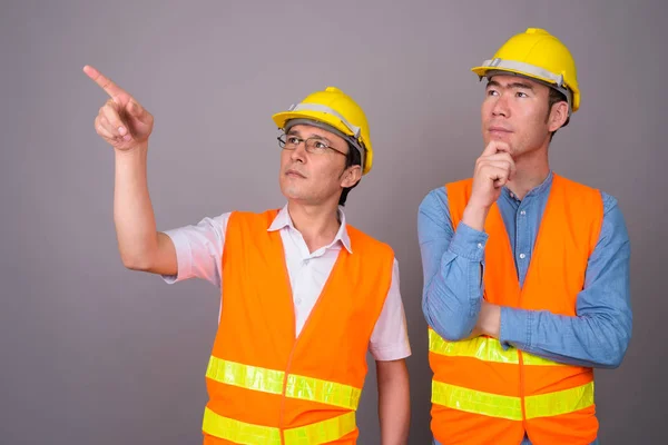 Dos jóvenes asiáticos trabajadores de la construcción juntos contra ba gris —  Fotos de Stock