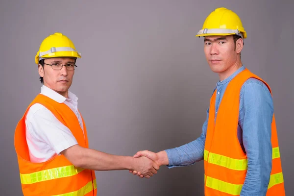Dos jóvenes asiáticos trabajadores de la construcción juntos contra ba gris —  Fotos de Stock